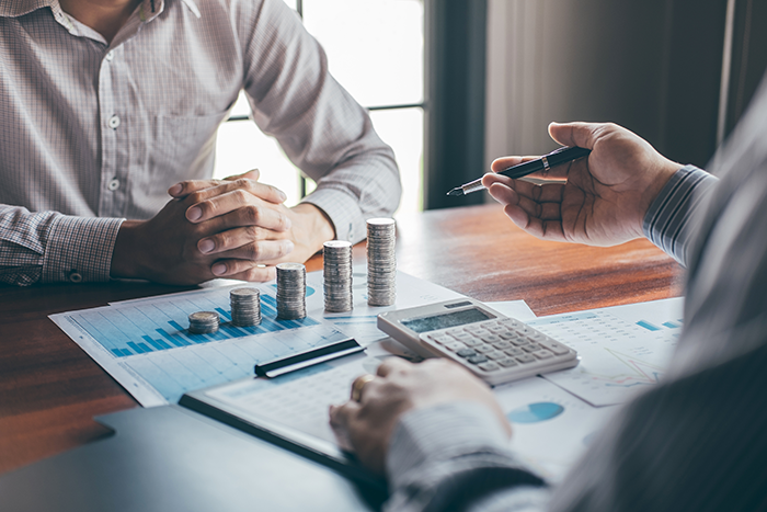 Banker with customer looking at financial graphs with coins and calculator on table